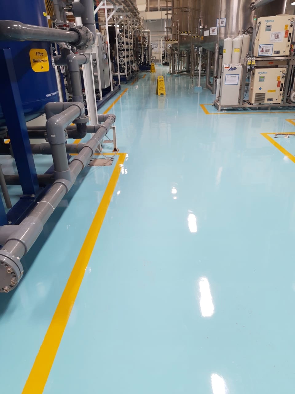 Corredor industrial com piso azul-claro e faixas amarelas