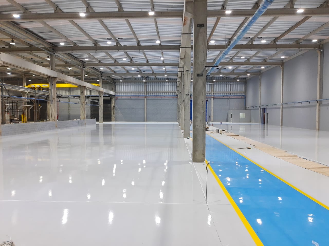 Piso industrial cinza com faixa azul e demarcação amarela